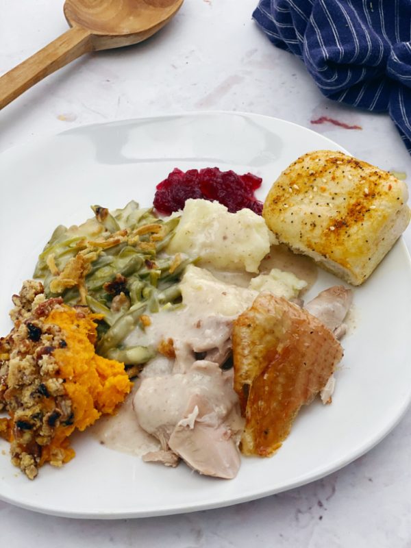 Plate of thanksgiving dinner with turkey sweet potatoes green beans cranberries mashed potatoes and a roll