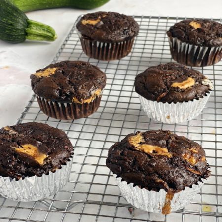 Chocolate zucchini muffins with peanut butter on cooling rack with zucchini