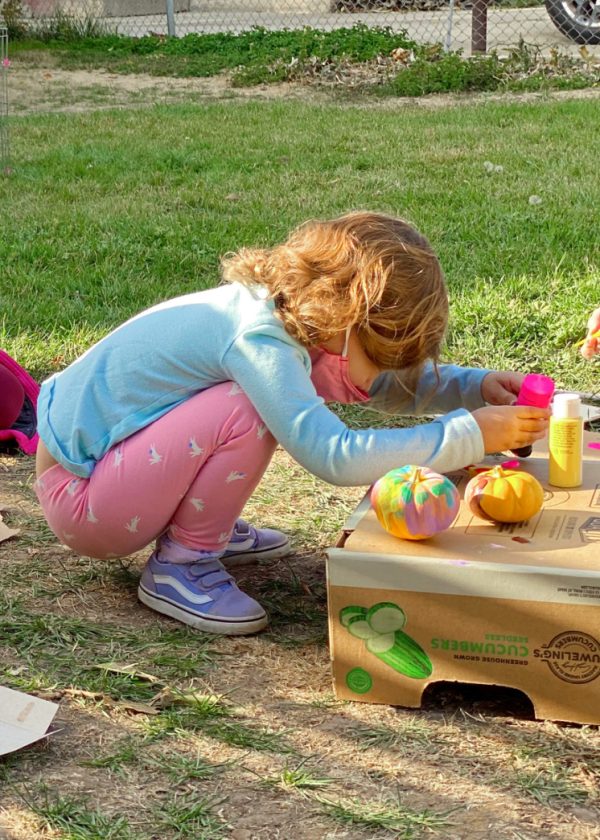 little girl painting mini pumpkins outside